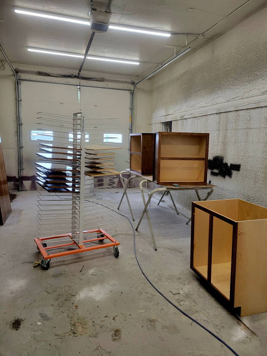 Cabinet doors and drawer fronts on a spray finishing rack in the shop, alongside a stripped cabinet box