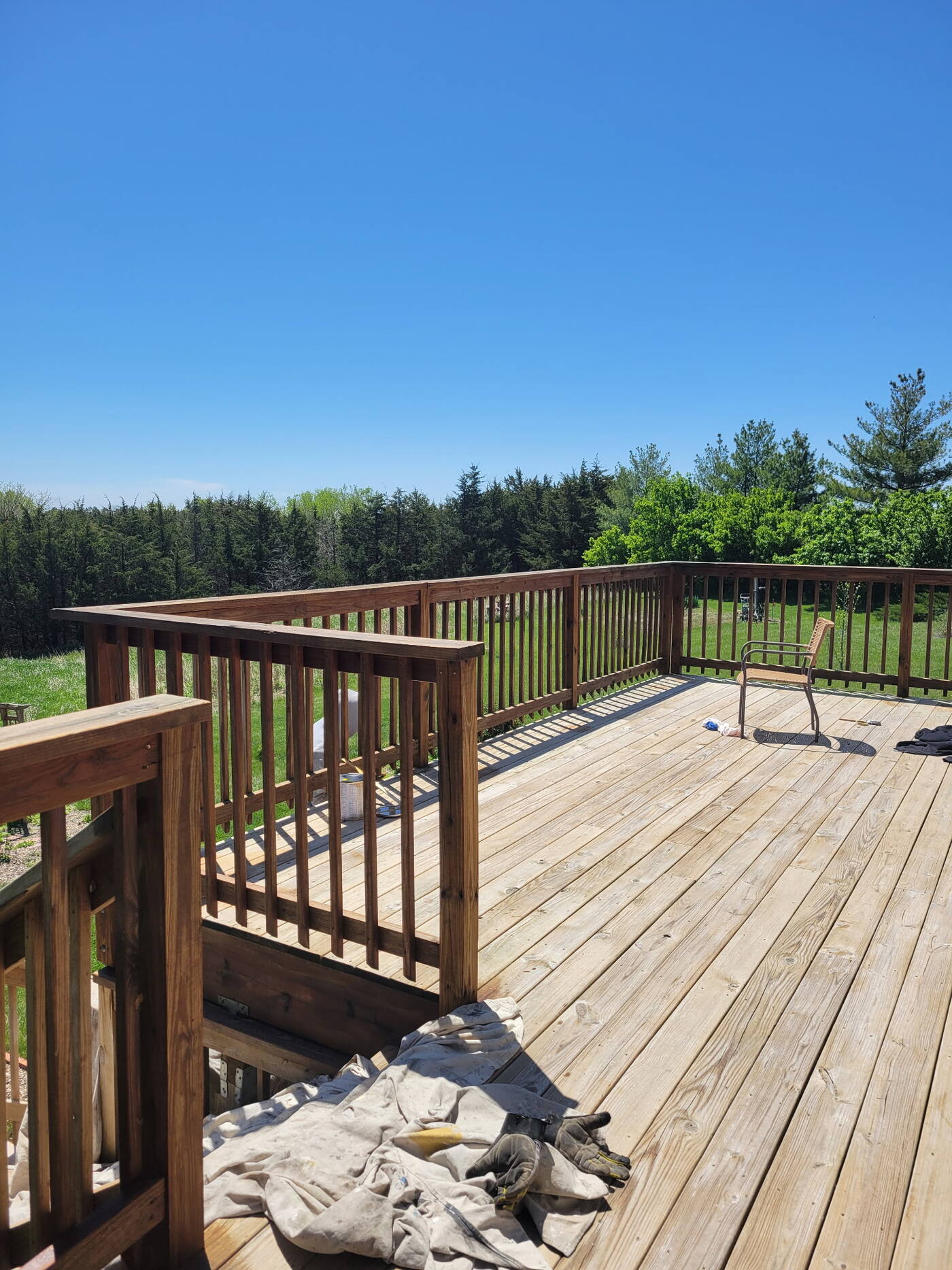 Wraparound deck with freshly stained dark railings and natural wood decking, overlooking an open field